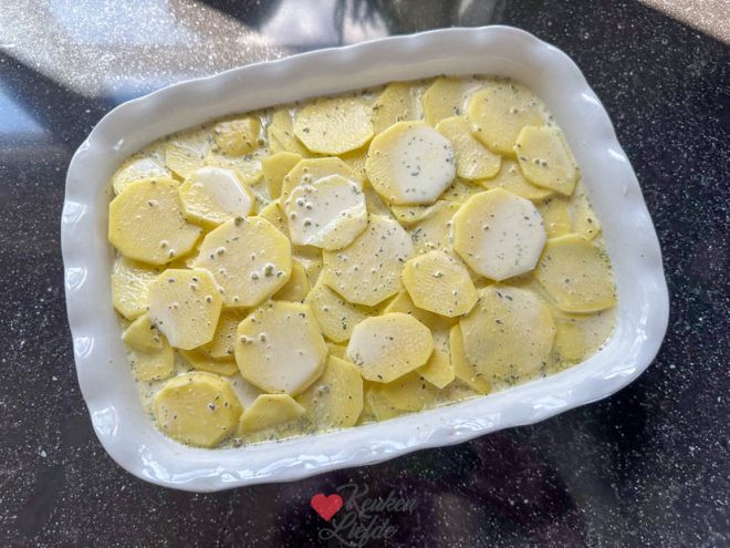 Dek de ovenschotel af met aardappelschijfjes en roomsaus